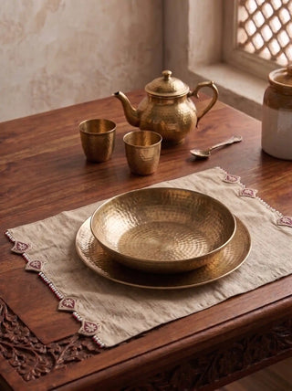 The Gulnaz hand-embroidered table mat styled under a hammered brass bowl and teapot set on a dark wood dining table.