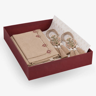 Gulnaz gift set in an open maroon box — folded beige linen table mats with maroon and ivory medallion embroidery, beside a round embroidered tieback with twin tassels
