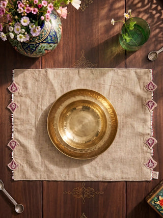 A top-down flatlay shot of the Gulnaz sand-beige linen table mat showing its symmetric pearl-and-ruby scalloped side borders.