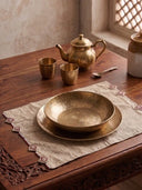Gulnaz embroidered table mats in cream linen with maroon teardrop motifs styled with hammered brass bowls and traditional tea service on dark wood.