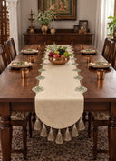 Gulnaz table runner down a long wooden dining table, with embroidered floral medallions, a tassel fringe and a brass bowl of fruit