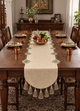 Gulnaz table runner down a long wooden dining table, with embroidered floral medallions, a tassel fringe and a brass bowl of fruit