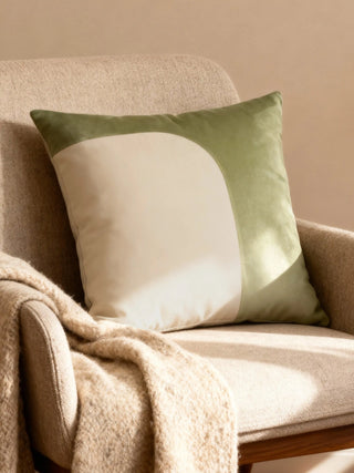 A luxury Half n Half cushion cover in sage green and ivory velvet with a curved color-block design resting on a textured beige armchair.
