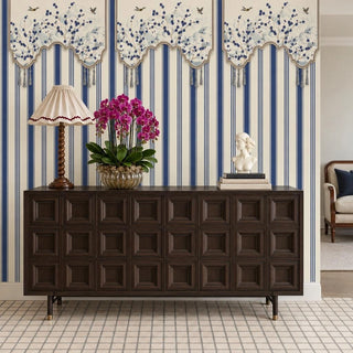 The Hana Stripes navy and ivory wallpaper on a foyer feature wall behind a dark wood sideboard with a twisted-wood lamp and magenta orchids view-foyer
