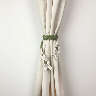 Floret Braid Handcrafted Curtain Tieback secured around a cream linen-look curtain, showcasing the contrast between the green braid and white flowers.