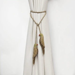 Handcrafted green parrot curtain tieback with gold embroidery holding back a white drape.