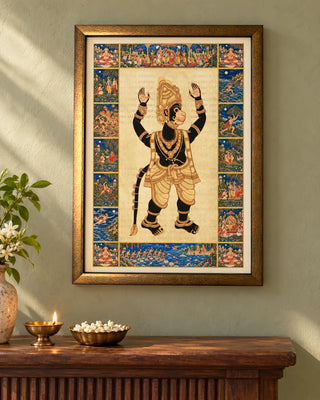 Hanuman Ansh framed wall art on a sage-green wall above a wooden console with a brass diya, a bowl of jasmine and a vase of white flowers.