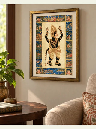Hanuman Ansh framed wall art in a living room beside a window, above a round wooden side table with a brass vase and a linen armchair.