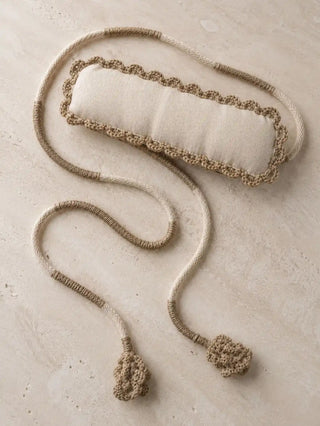 A flat lay view of the Hazel Verse curtain tie back on a limestone surface showcasing its padded linen band, scalloped crochet trim, and long wrapped cords.