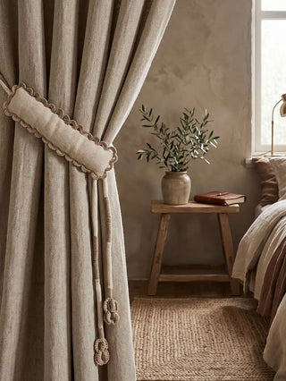 The Hazel Verse custom drapery tie back styled seamlessly over a heavy greige linen curtain in a warm, textured cottage bedroom sanctuary.