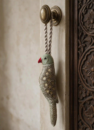 The Heer charm in Sage & Gold, view-doorknob hanging from a brass knob beside a carved wood panel.