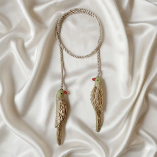 Flat lay view of a pair of embroidered heer bird curtain tiebacks with braided rope on a silk background
