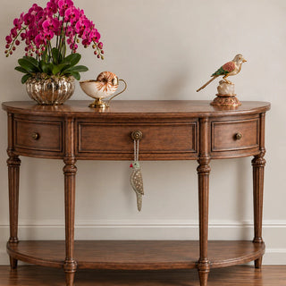 The Heer Parrot Hanging Gift Charm hanging from a round brass knob on a walnut console table with a bowl of magenta orchids.