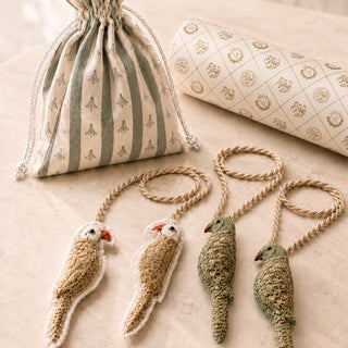 Heer and Ranjha embroidered bird tiebacks in both colourways styled beside a striped drawstring gift pouch