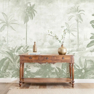 The Hidden Grove sage green tropical mural styled in a luxury living room behind a vintage wooden console table.