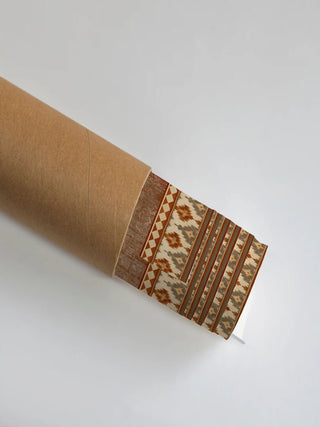 The Ikat Fusion wall art print partly unrolled from its shipping tube, showing a distressed rust texture panel beside an ikat diamond stripe in rust and cream.