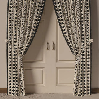 The Ikkat Fringes curtain in a room setting, hanging to one side and styled with a wooden chair and side table, showcasing its full length.