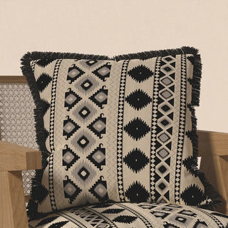 The "Ikkat Fringes" cushion cover displayed on a light wooden chair, showcasing its striking bohemian style and how it adds contrast to a home setting.