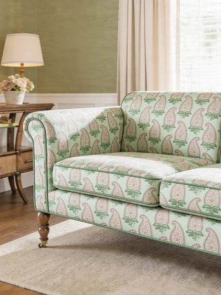 A luxury sofa upholstered in Indian Paisley fabric featuring a pink and green paisley pattern on a mint base against a sage green wall.