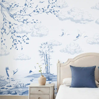 Indigo Whisper Wallpaper: Full mural installation of the light blue and white scenic wallpaper featuring cranes and blooming branches above a bed.