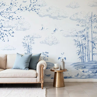 Living room with a beige sofa, decorative pillows, and a small table against a wall with blue floral wallpaper.