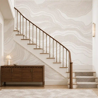 Infinite Flow abstract wallpaper in Ivory Sand lining a staircase wall beside a wooden console and lamp.
