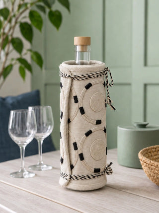 Ivory Blossoms jug cover wrapped around a glass water carafe with wine glasses on a light wooden table.