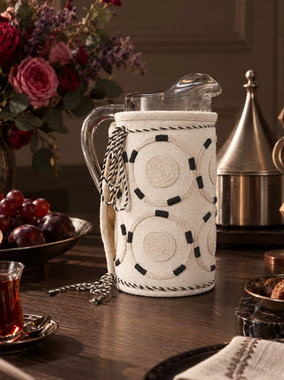 Ivory Blossoms jug cover on a glass pitcher set on a dark wood dining table with fresh roses and silver cloche