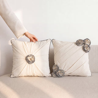 Styled pair of Ivory Gardenia draped pillows with gathered fabric centers, charcoal piping, and metallic twisted rose embellishments on cream upholstery.
