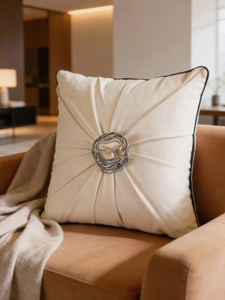 A luxury ivory pleated cushion cover with a central grey corded rose rosette styled on a tan leather armchair.