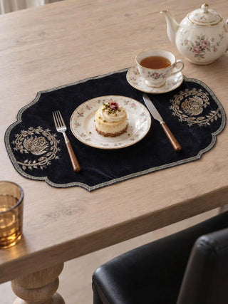 Jashn navy table mat used as a place mat on a light oak table, under a floral porcelain plate with a small dessert, a teacup, and a fork and knife with wooden handles.