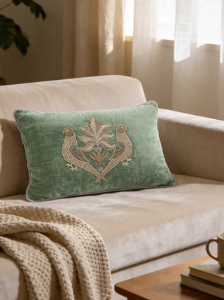 A luxury pistachio green velvet cushion with parrot embroidery styled on a beige velvet sofa with a cream knit throw.