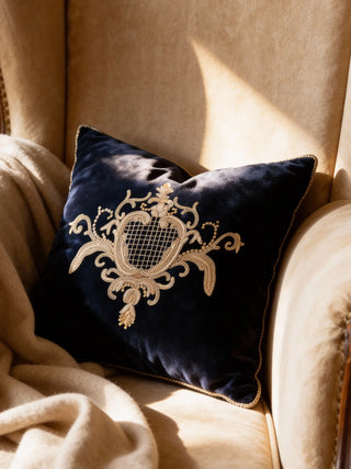 A luxury Jewels of Nizam cushion in navy velvet with a gold-embroidered royal crest resting on a tan wingback chair.