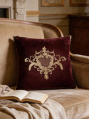 The Jewels of Nizam cushion styled on a beige velvet armchair next to an open book.