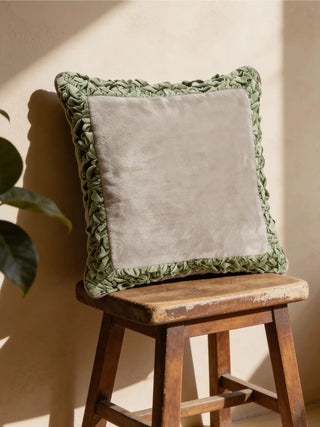 A Jhalak ivory and green cushion resting on a rustic wooden stool in warm sunlight.