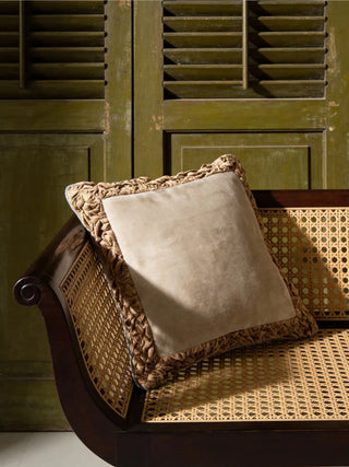 The Jhalak ivory and peach cushion styled on a natural wicker chair with a warm throw.