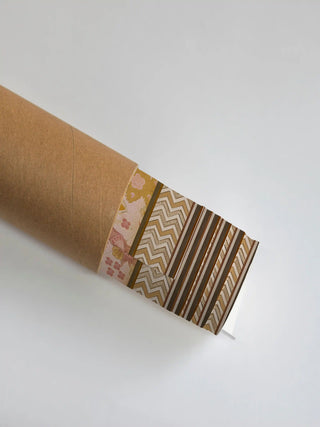 The Kahani wall art print partly unrolled from its shipping tube, showing a pink floral panel beside a chevron zigzag border and stripes in mustard and brown.