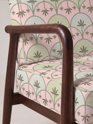 Detail of the Kanan upholstery fabric in pink and green on a walnut-framed armchair, showing the piped seams and scalloped arch pattern in a living room.