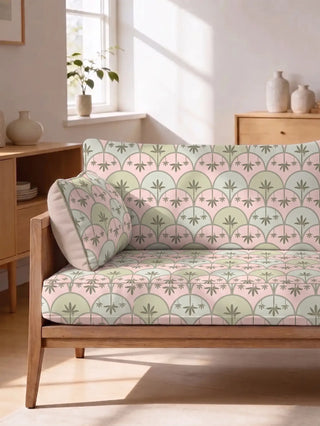 Kanan upholstery fabric in pink and green on a light oak sofa with a matching bolster cushion, in a sunlit living room with pale wood cabinets and ceramic vases.