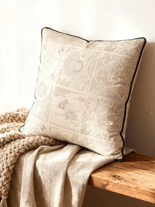 A luxury Kantha cushion cover featuring hand-guided narrative embroidery on sand linen resting on a rustic wooden bench.