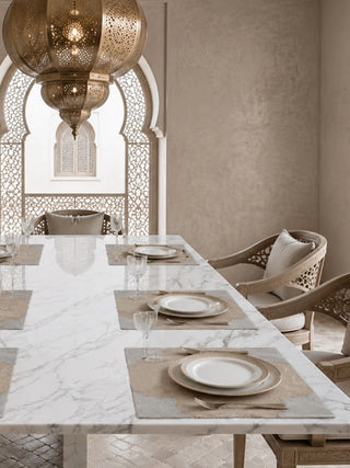 Kasbah Pearl placemat set displayed on a white marble dining table under a carved brass lantern in a courtyard setting.
