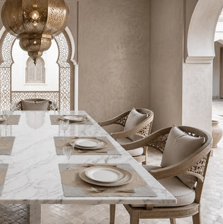 The Kasbah table mats set on a marble dining table with carved wooden chairs in an arched Moroccan-style dining room