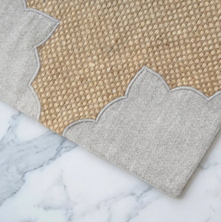 Close up of the scalloped grey felt edge and woven jute texture of The Kasbah table mat on a marble surface