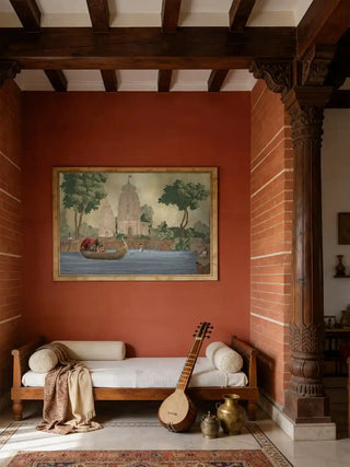 Kashi Reverie temple and swan boat wall art in antique sepia, framed in pale gold on a terracotta wall above a wooden daybed with bolsters and a veena in a beamed living room.