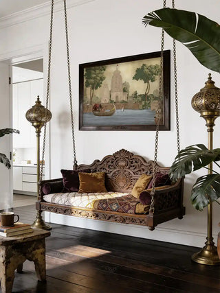 Kashi Reverie riverside temple wall art in antique sepia, framed in dark wood above a carved wooden swing with velvet cushions and brass floor lamps in a living room.