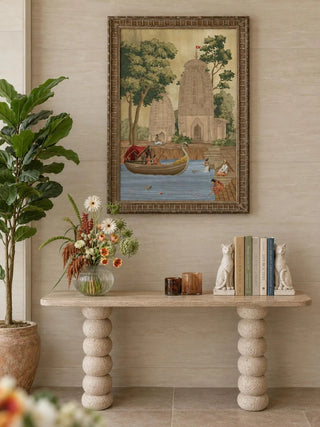 The Kashi Reverie wall art in a carved wood frame above a travertine console with a flower vase, candle holders and cat bookends.