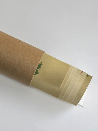 The Kashi Reverie wall art partially unrolled from its kraft paper shipping tube, showing green foliage on a warm ochre ground.
