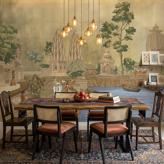 The Kashi Reverie wallpaper mural in a room, showing a detailed scene with a temple by the water and a devotee, in golden sepia colors view-diningnroom