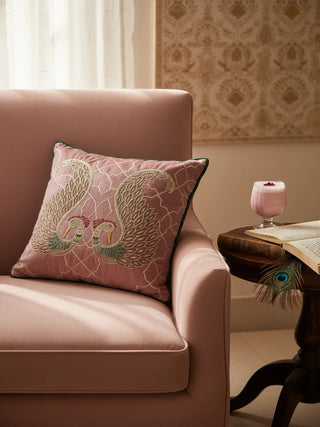 A luxury mood shot of the Kashmir cushion in dusty rose styled on a pink velvet armchair next to a vintage book.