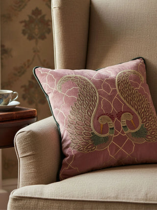 The Kashmir cushion featuring hand-embroidered bird motifs styled on a classic beige wingback chair with a side table.